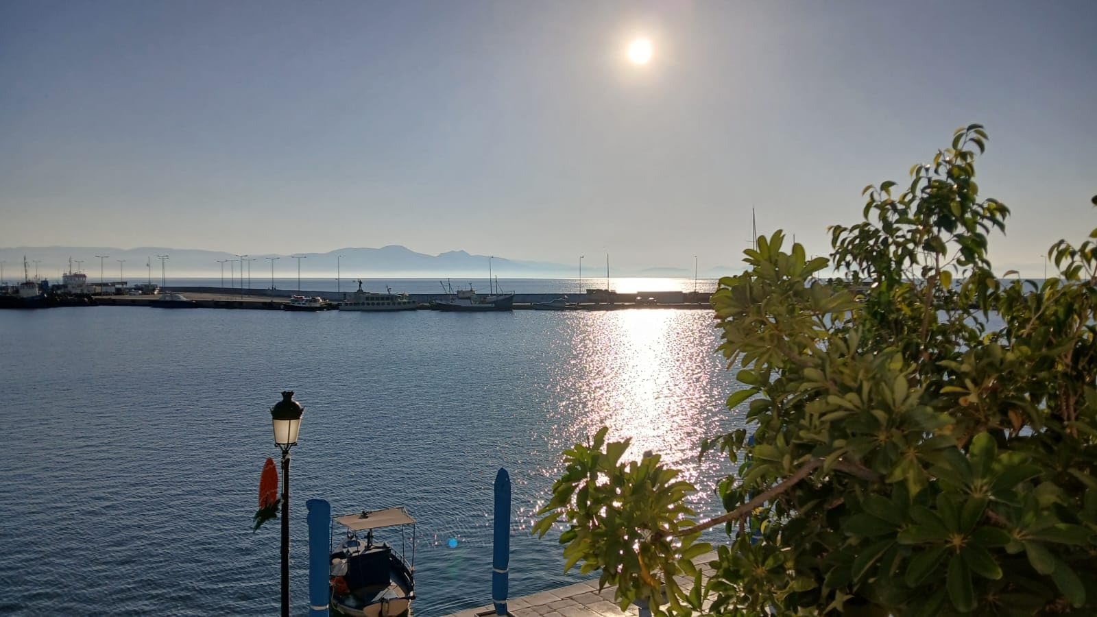 Hazy sunshine reflected over see and harbour with mountains in background